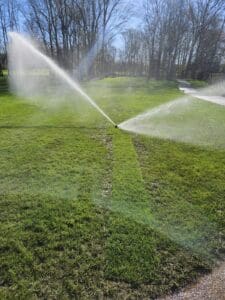 A couple of water sprinklers spraying on some grass.