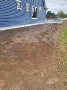 A dirt yard with blue house and grass